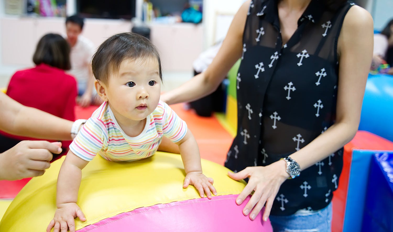A mother assisting her toddler on soft play equipment